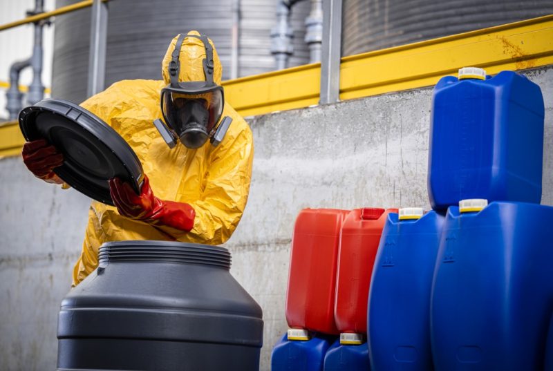 Working in chemical factory. Experienced worker in protection suit and gas mask opening barrels with acid.
